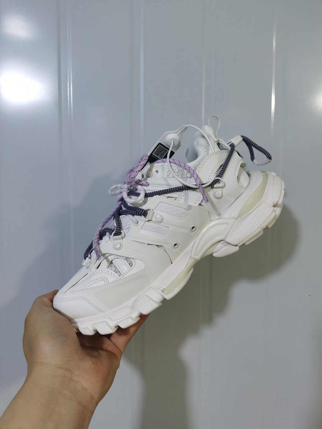 Side and underside view of the white Balenciaga sneaker, showing the panel construction, heel shape, and textured outsole.