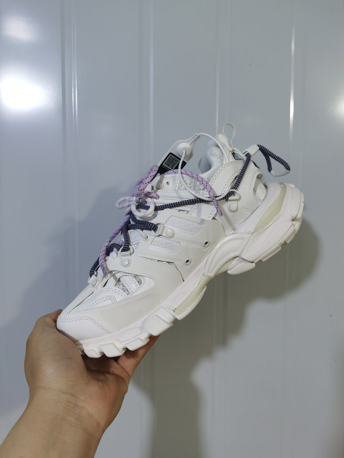 Side and underside view of the white Balenciaga sneaker, showing the panel construction, heel shape, and textured outsole.