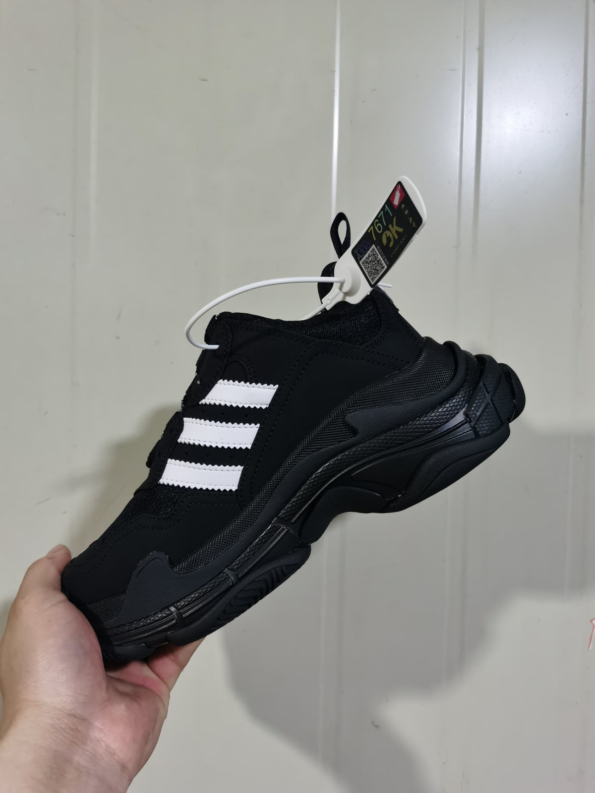 Side and outsole view of the black and white Balenciaga Triple S sneaker, showing its layered construction, textured sole, and attached product tag.