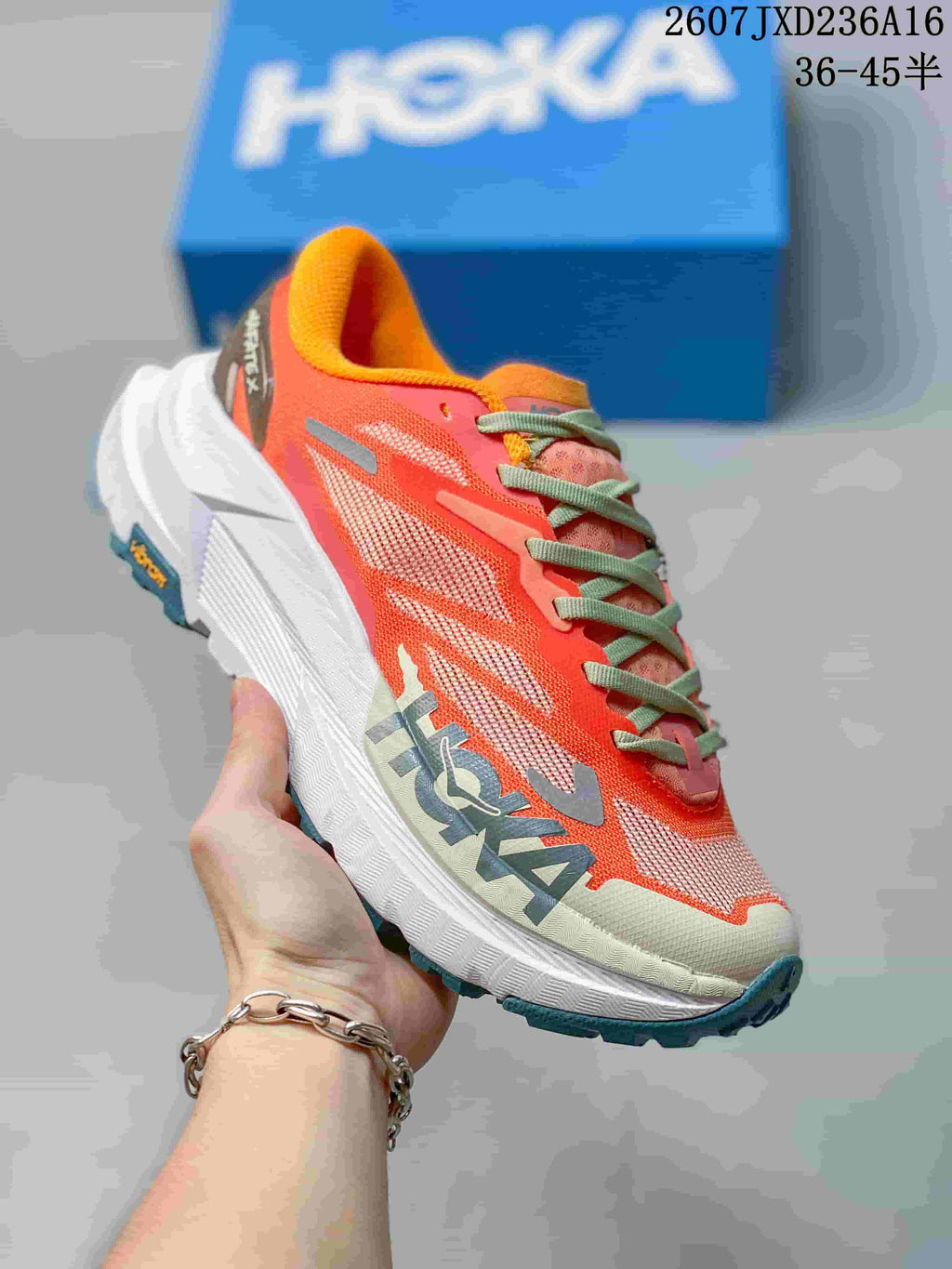 Angled side view of the coral Hoka MAFATE X shoe showing the layered upper, high-profile white midsole, and teal outsole.