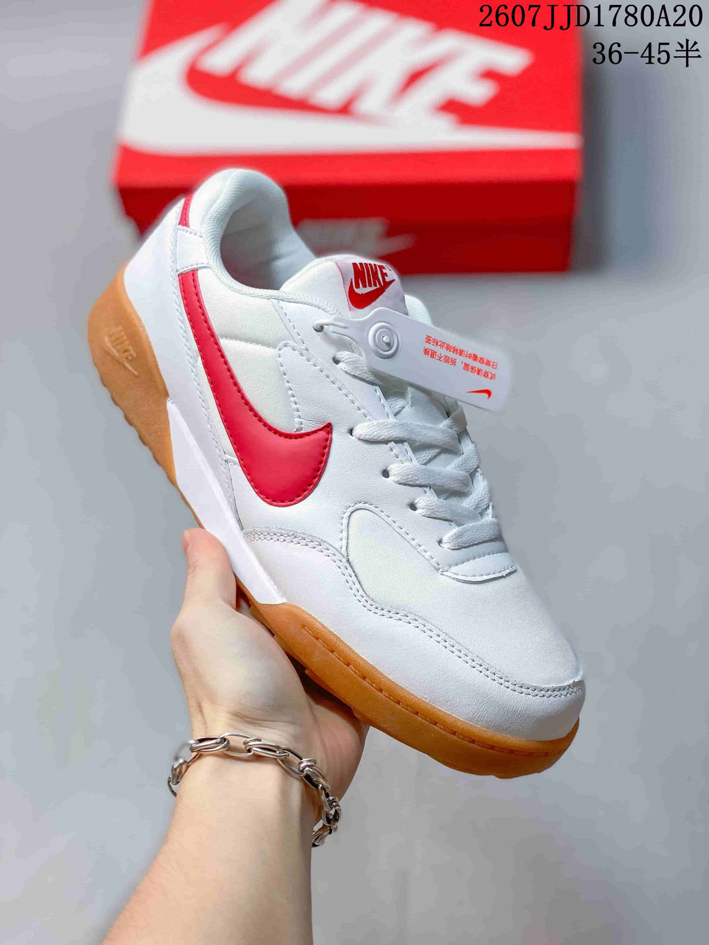 Angled side view of the white and red sneaker with its gum-colored sole and layered upper panels.