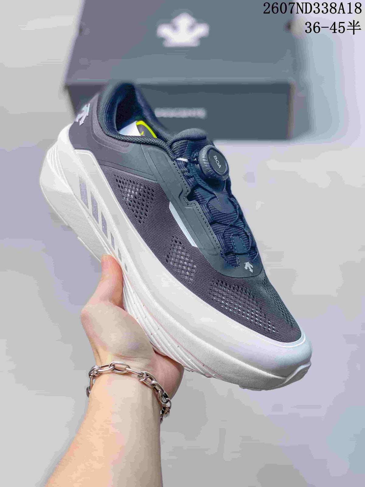 Side view of a black Descente sneaker held in hand, showing the perforated upper, dial closure and layered sole.