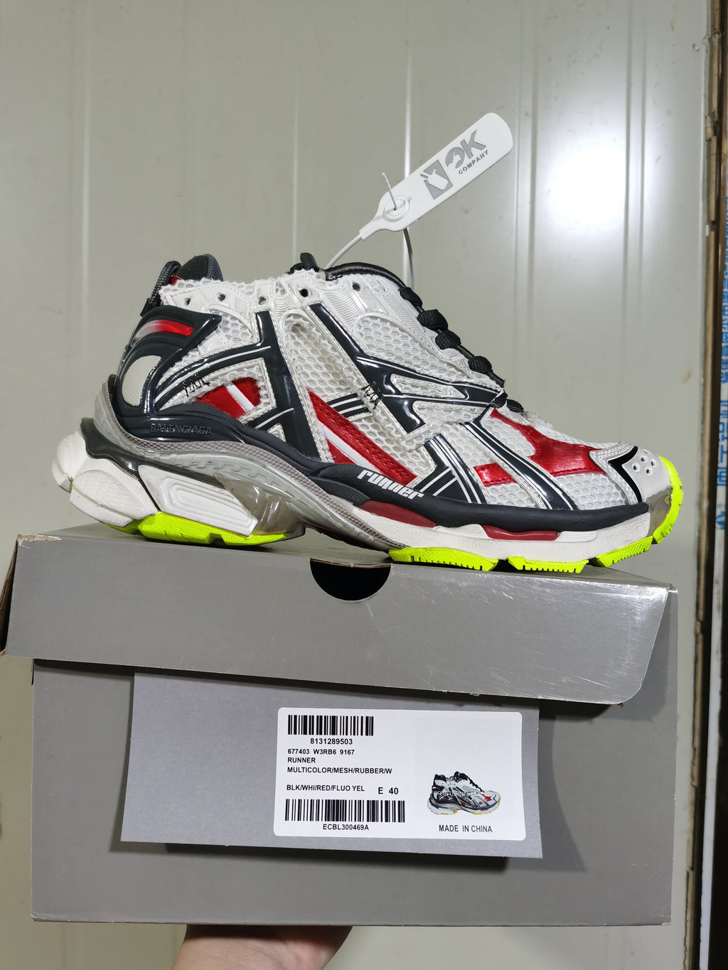 Balenciaga Runner sneaker displayed on its box, with the label showing style code 677403 W3RB6 9167, color code BLK/WHI/RED/FLUO YEL and size E 40.