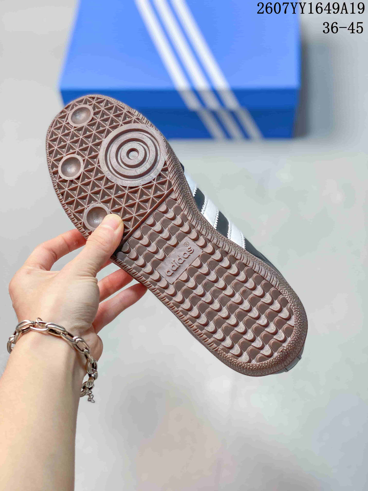 Close view of the brown gum-colored outsole showing a geometric tread pattern and adidas branding; the background includes an adidas shoe box.