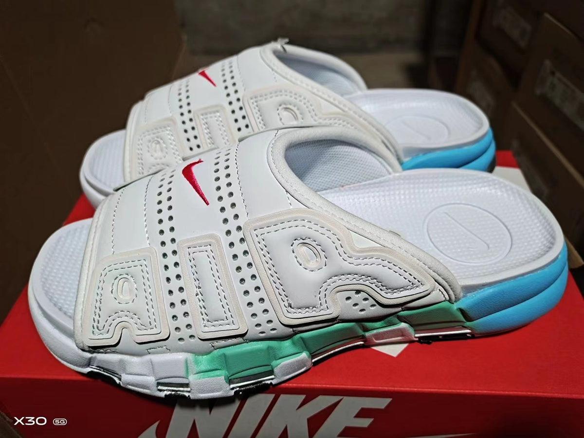 White Nike Air-style slide sandals with red branding details, a white upper, and green and blue outsole accents.