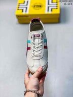 Front view of a white lace-up Onitsuka Tiger sneaker with burgundy and turquoise side details.