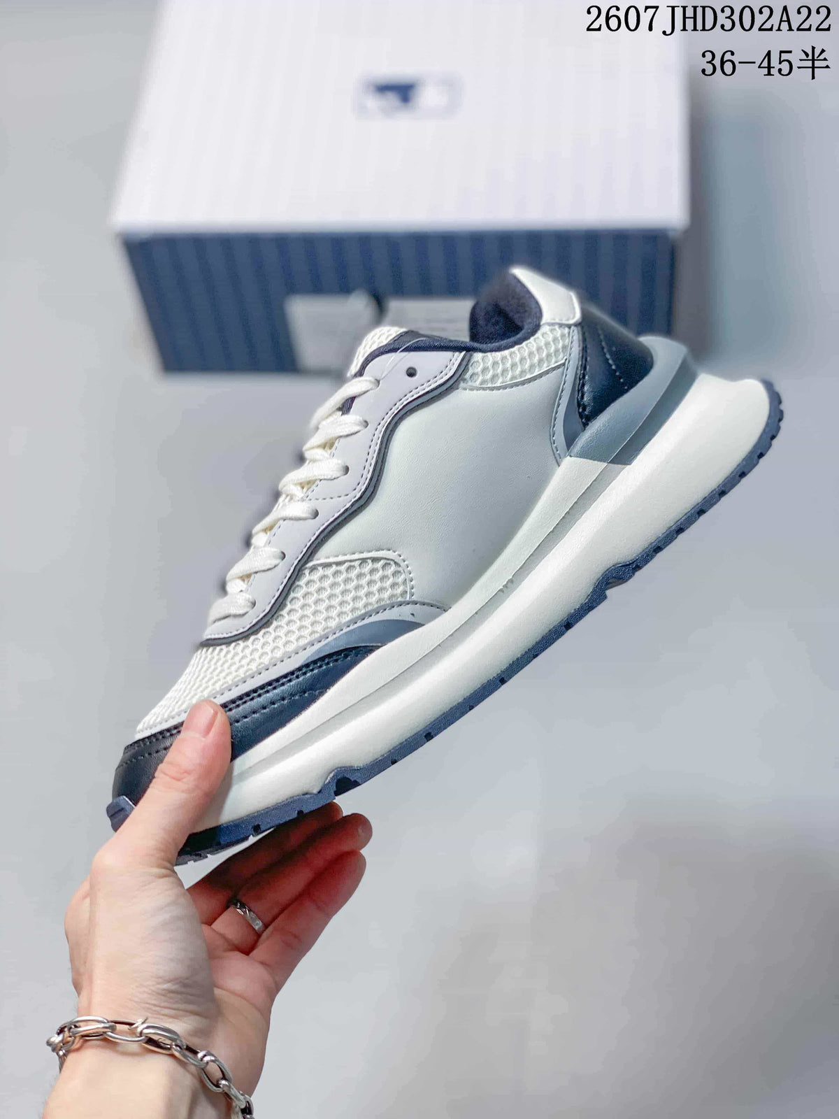 Side profile of the white and navy low-top sneaker showing the layered upper, mesh-look panels, and raised sole.