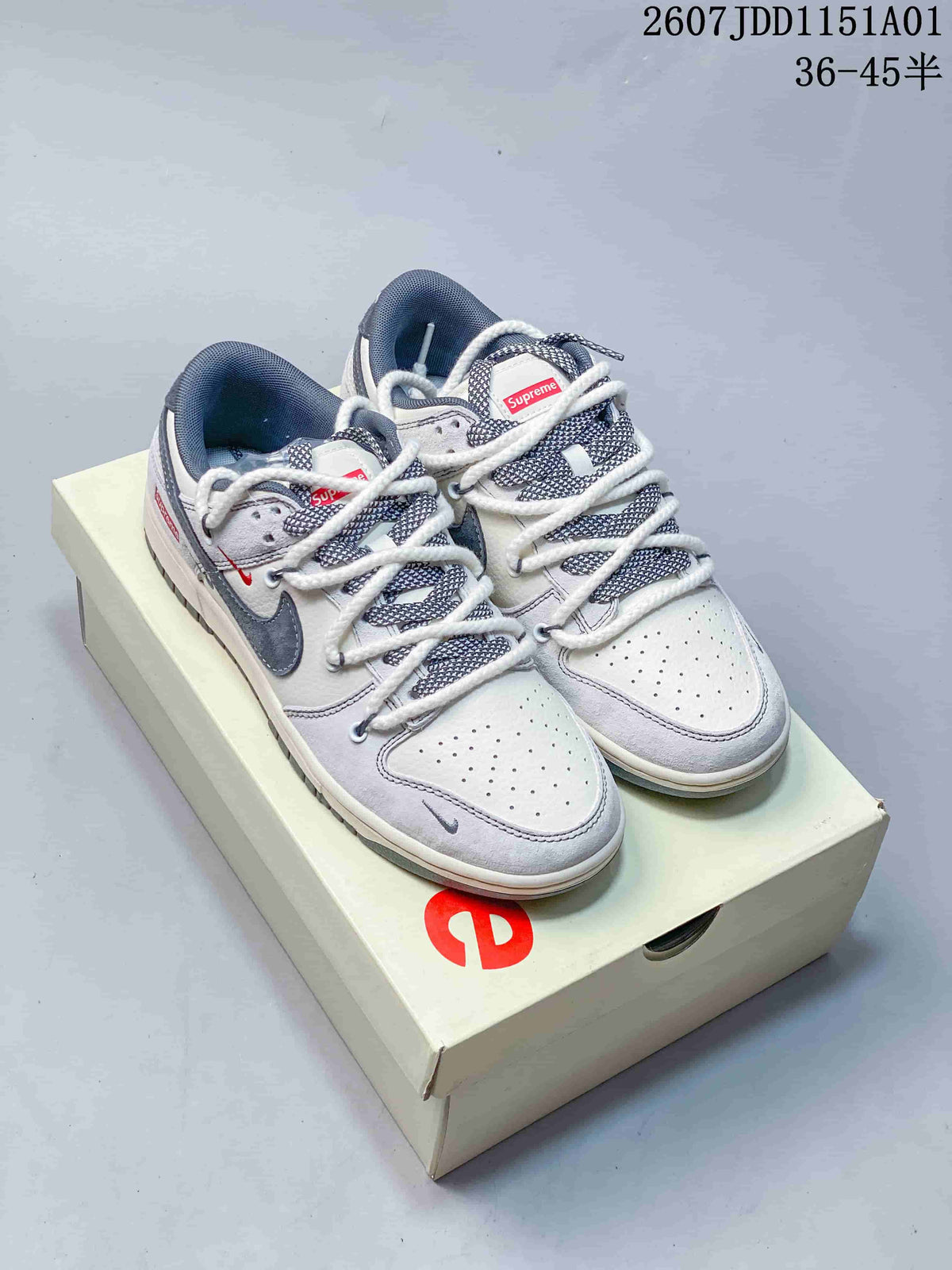 Pair of white and gray low-top sneakers with dark swoosh accents and patterned laces on a branded box.