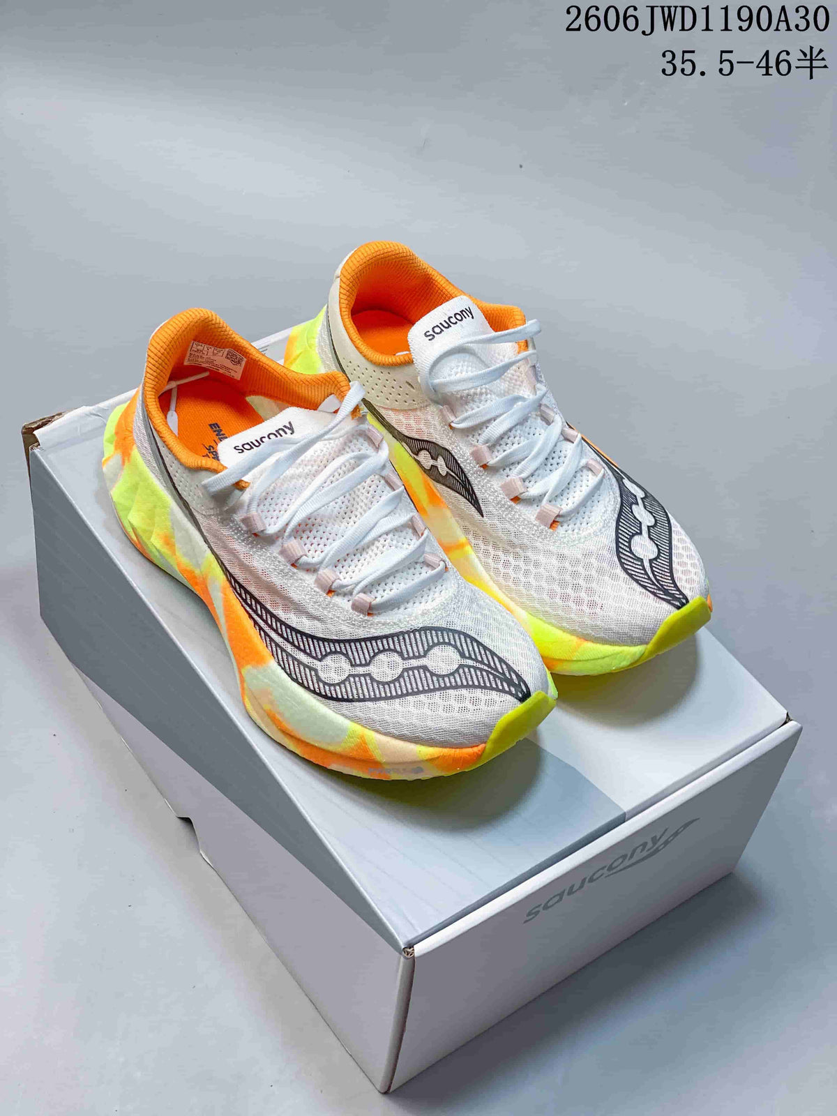 Pair of white Saucony Endorphin Pro running shoes with orange collars and neon yellow-green and orange accents, displayed on a shoe box.