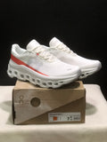 Pair of white and coral On Cloudmonster 1 sneakers displayed on a product box.
