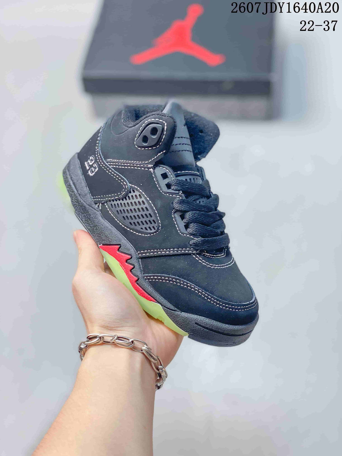 Angled side view of the dark Jordan sneaker showing the ankle panel, side ventilation-style panel, red accent, and translucent outsole.