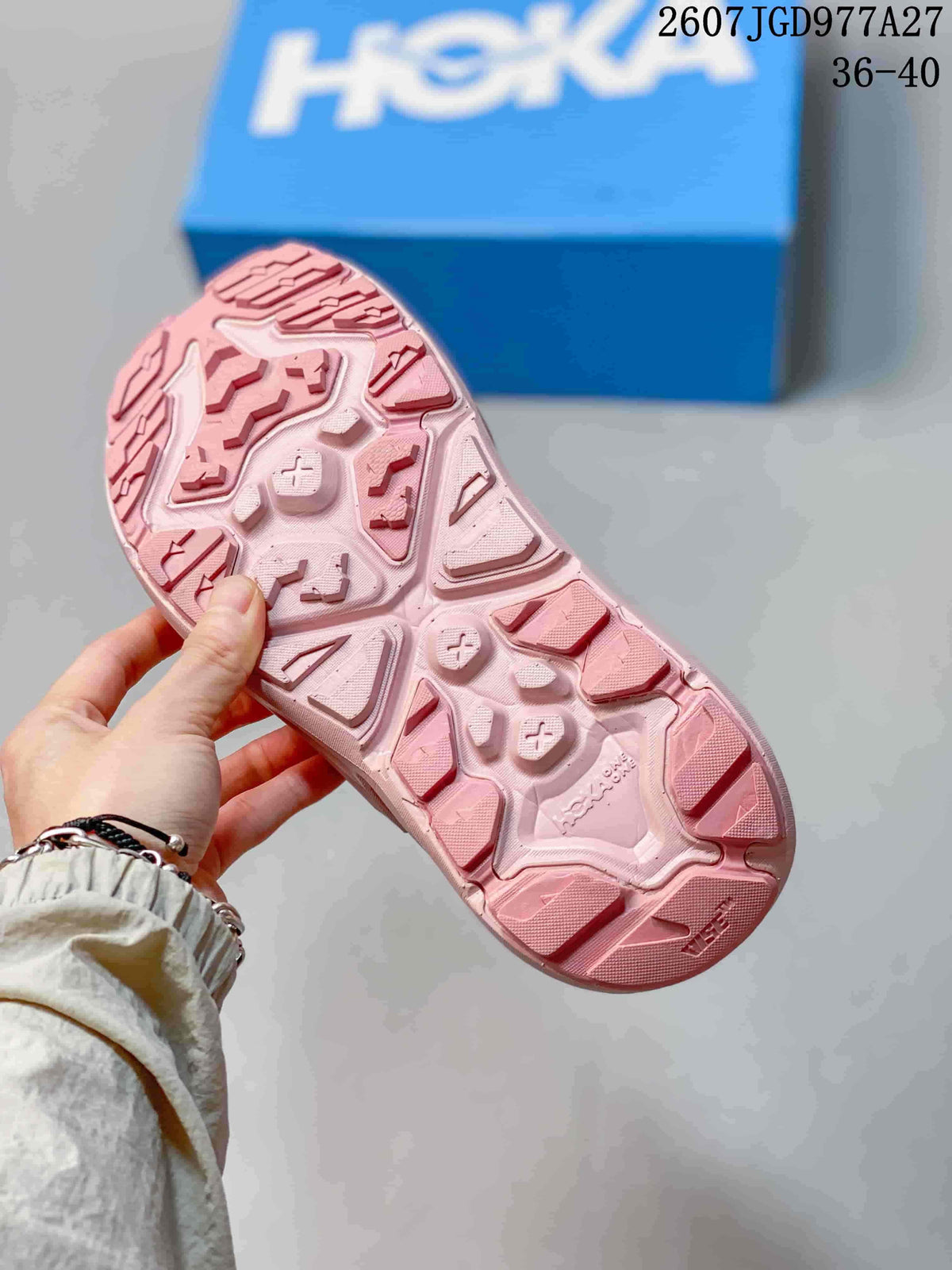 Pink HOKA sandal outsole showing a raised lugged traction pattern; overlay shows code 2607TGD977A27 and size range 36–40.