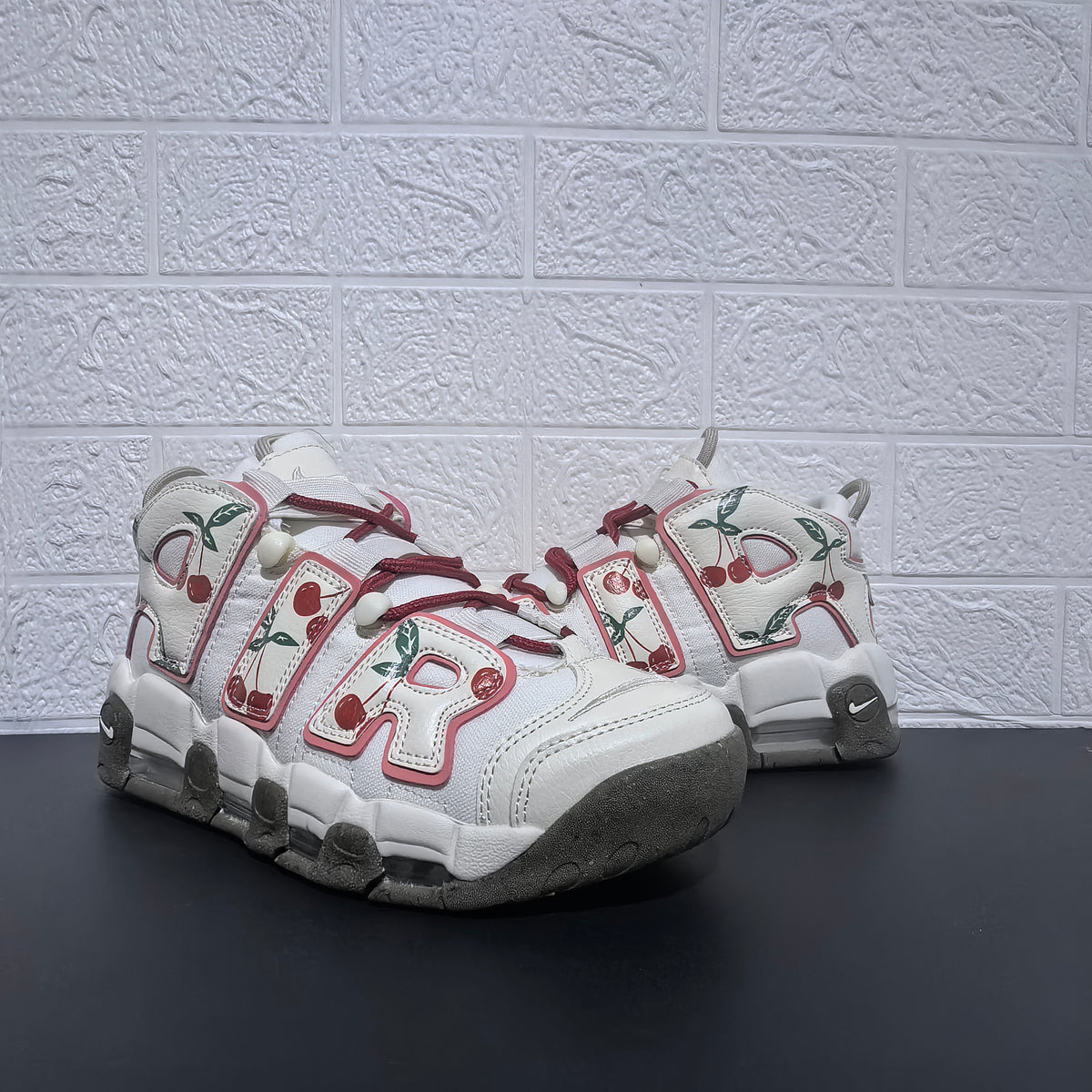Front three-quarter view of white sneakers with oversized cherry-patterned AIR lettering