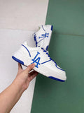 White low-top sneakers with blue LA-style lettering, blue laces, and blue outsole accents.
