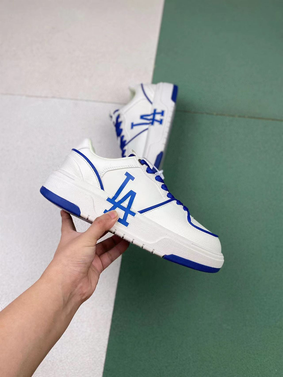 White low-top sneakers with blue LA-style lettering, blue laces, and blue outsole accents.