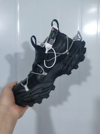Angled view of a black Nike sneaker showing the layered upper, pull tabs, cord overlays, and deep outsole tread.