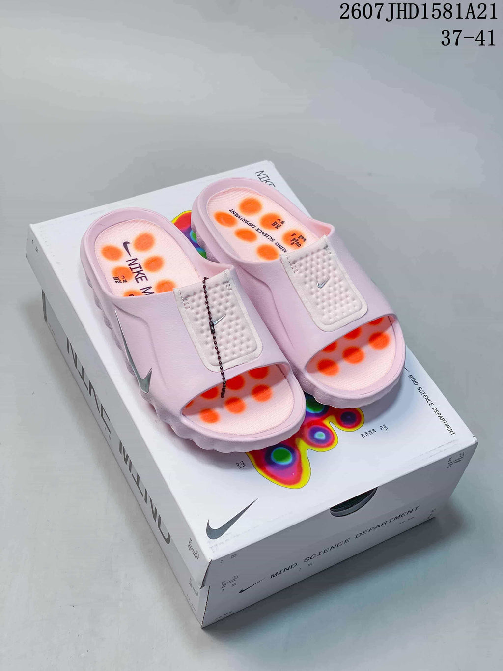 Pair of light pink Nike Mind mule slides displayed on a Nike Mind box, with orange outsole pods visible.