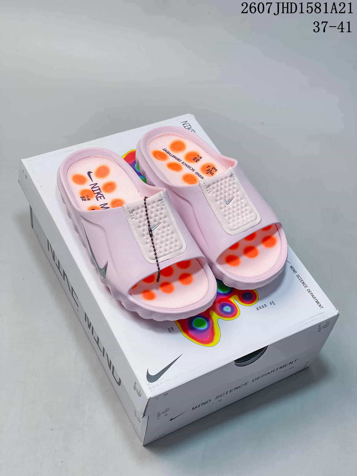 Pair of light pink Nike Mind mule slides displayed on a Nike Mind box, with orange outsole pods visible.