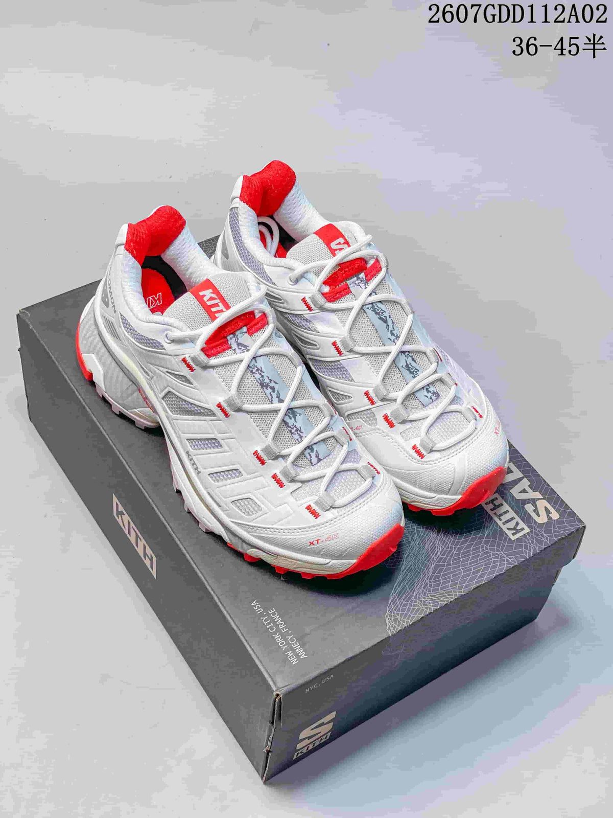 White and red and dark navy and red Salomon XT-4K sneakers displayed on a Kith-branded box.