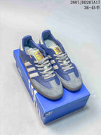 Blue adidas Samba sneakers displayed on a blue shoebox with light contrast stripes and textured toe panels.