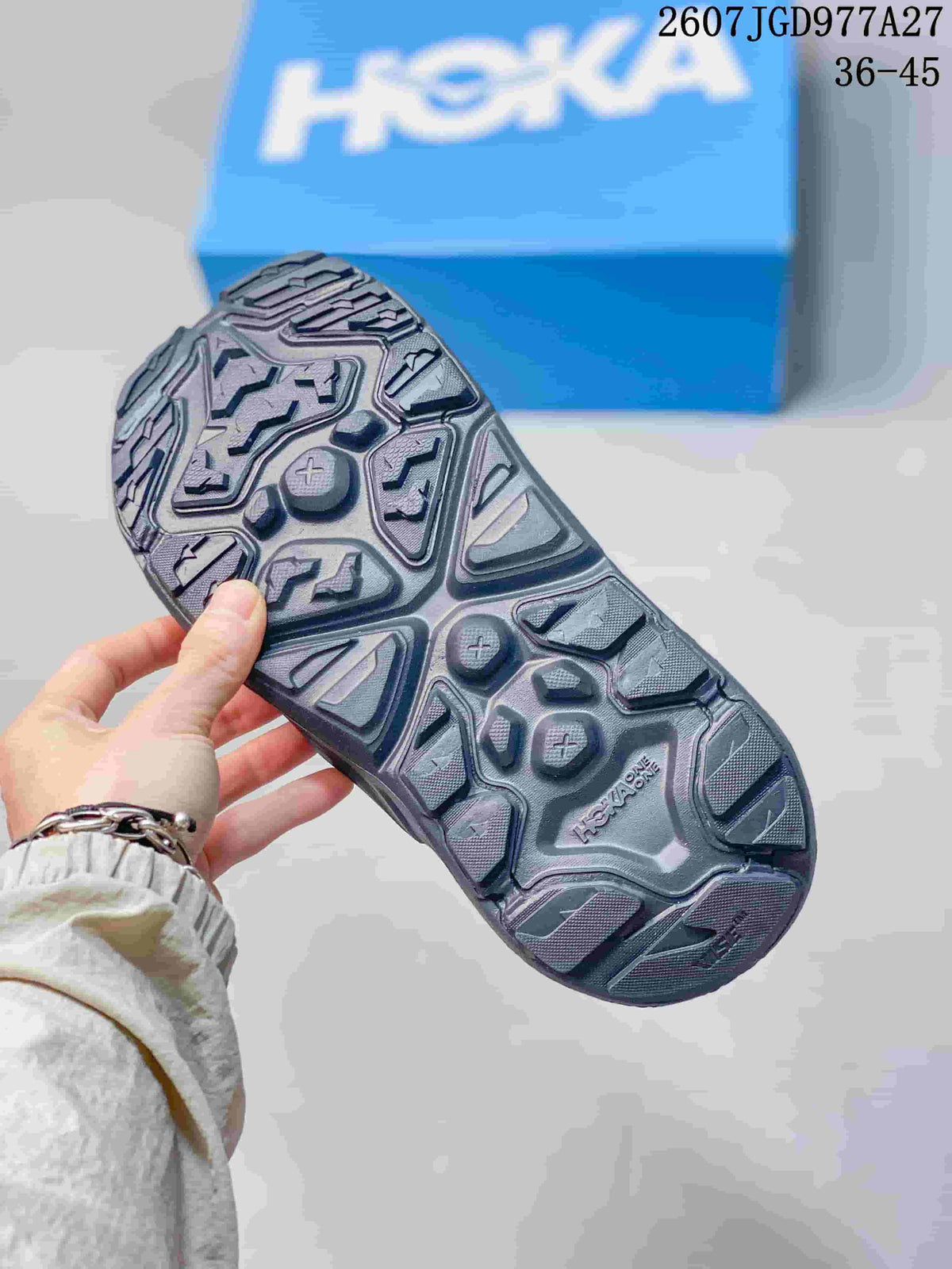 Close-up of the patterned outsole on a black HOKA Hopara OG sandal, showing raised tread sections and HOKA branding.