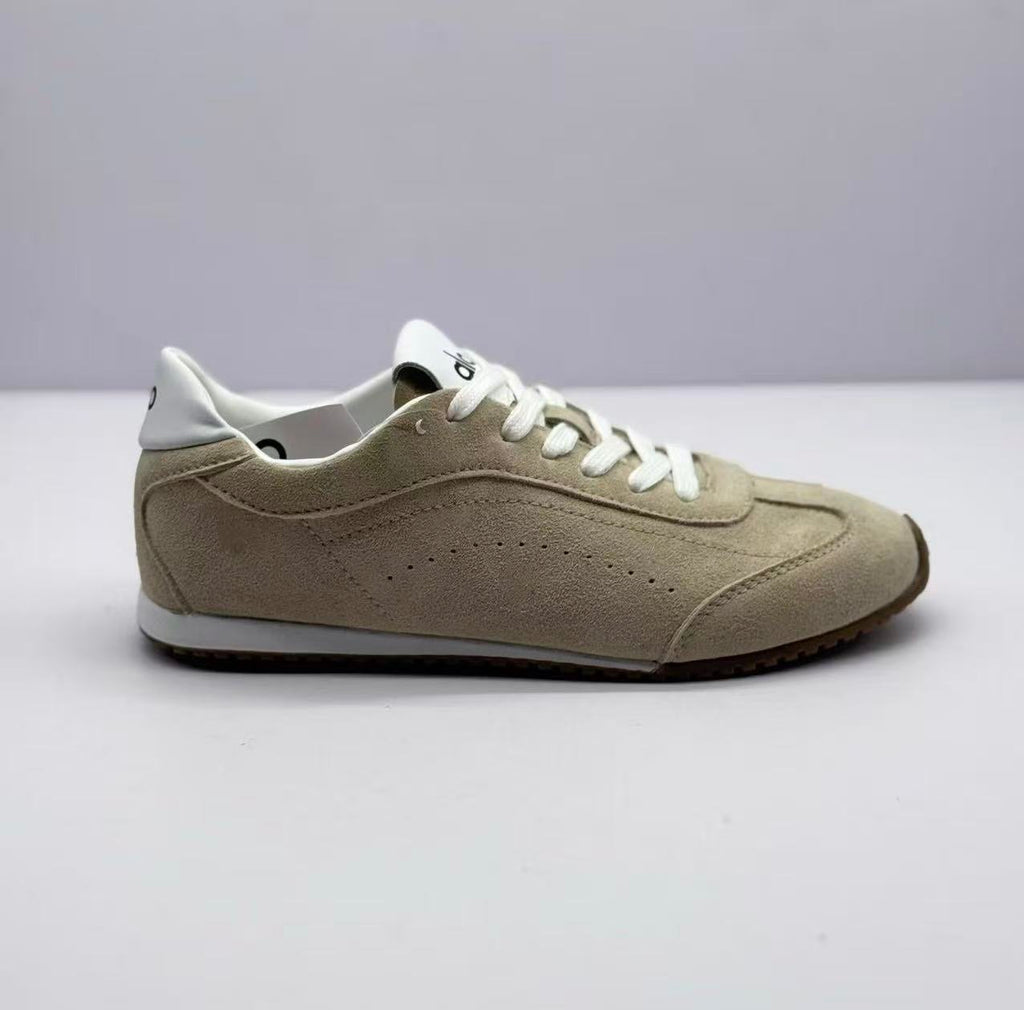 Side profile showing the beige sneaker's stitched panels, white collar and brown outsole.