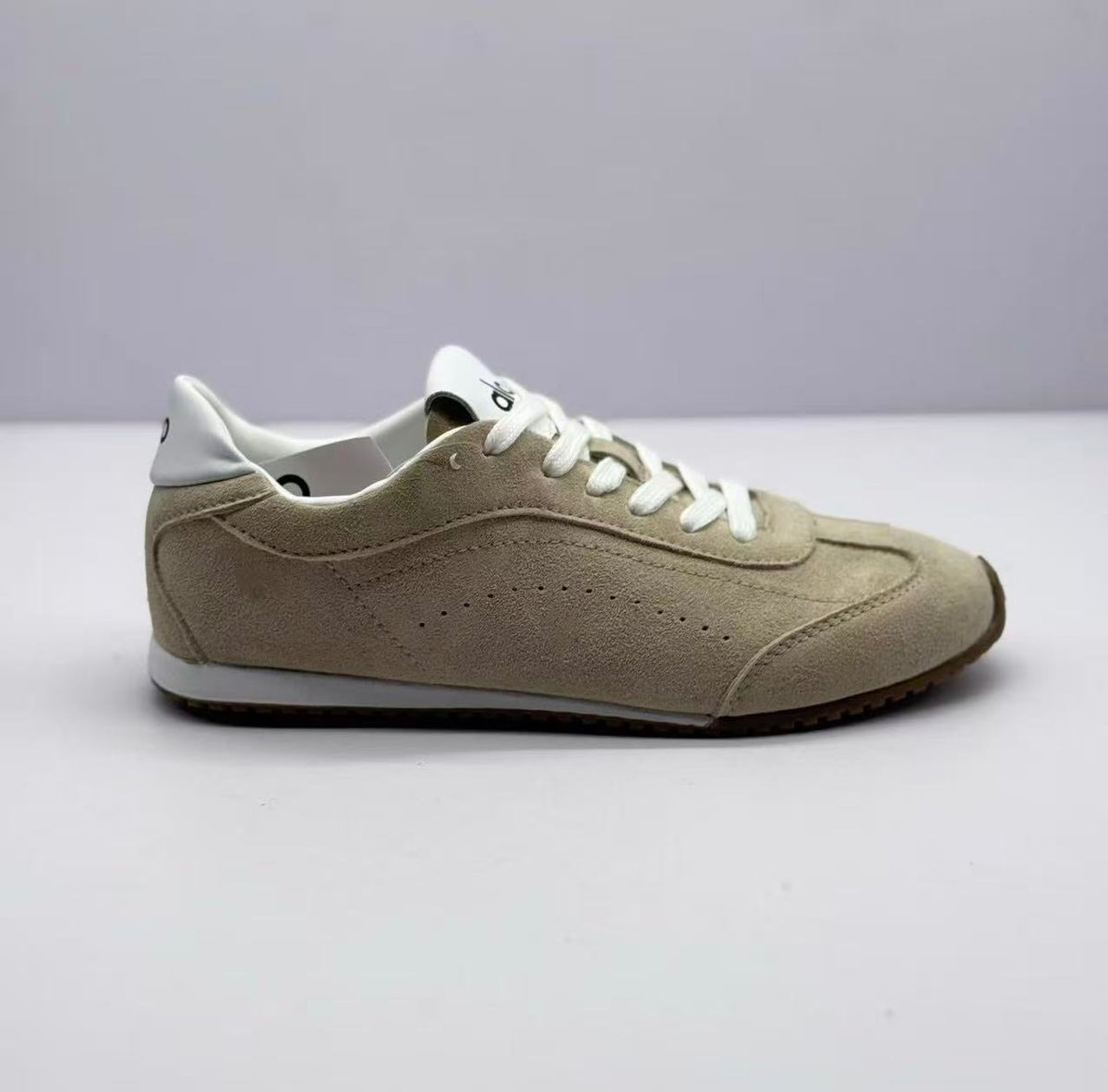 Side profile showing the beige sneaker's stitched panels, white collar and brown outsole.