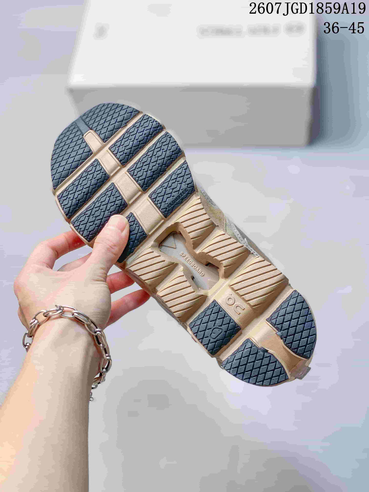 Underside view of a beige sneaker showing the segmented outsole, dark traction sections, and visible On branding.