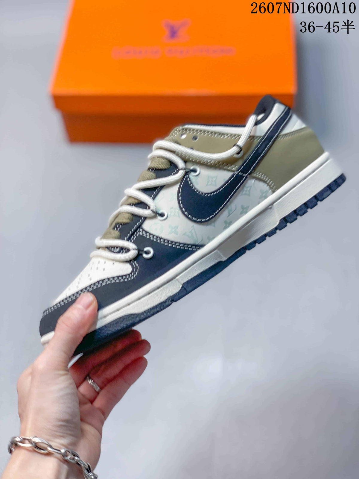 Side view of the low-top sneaker showing layered panels, contrast stitching, a dark side emblem, and an olive heel section.
