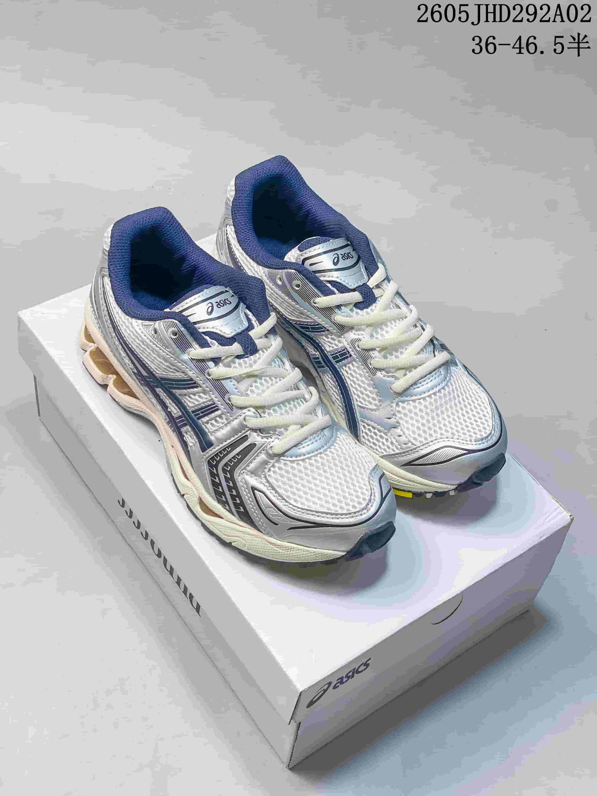 Pair of silver-toned ASICS GEL-KAYANO 14 sneakers with dark blue accents, shown on a shoebox