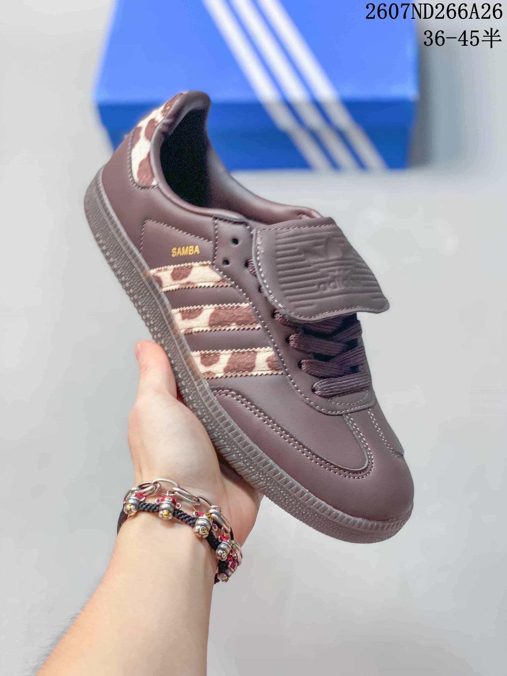 Side view of a brown adidas Originals Samba sneaker showing the three-stripe panel, Samba branding, flap tongue, laces, and textured outsole.