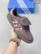 Side view of a brown adidas Originals Samba sneaker showing the three-stripe panel, Samba branding, flap tongue, laces, and textured outsole.