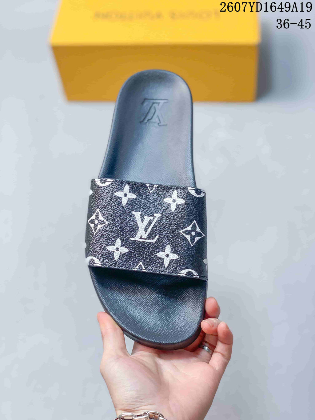 Top view of a black slide sandal with a white monogram-patterned strap and embossed footbed branding.