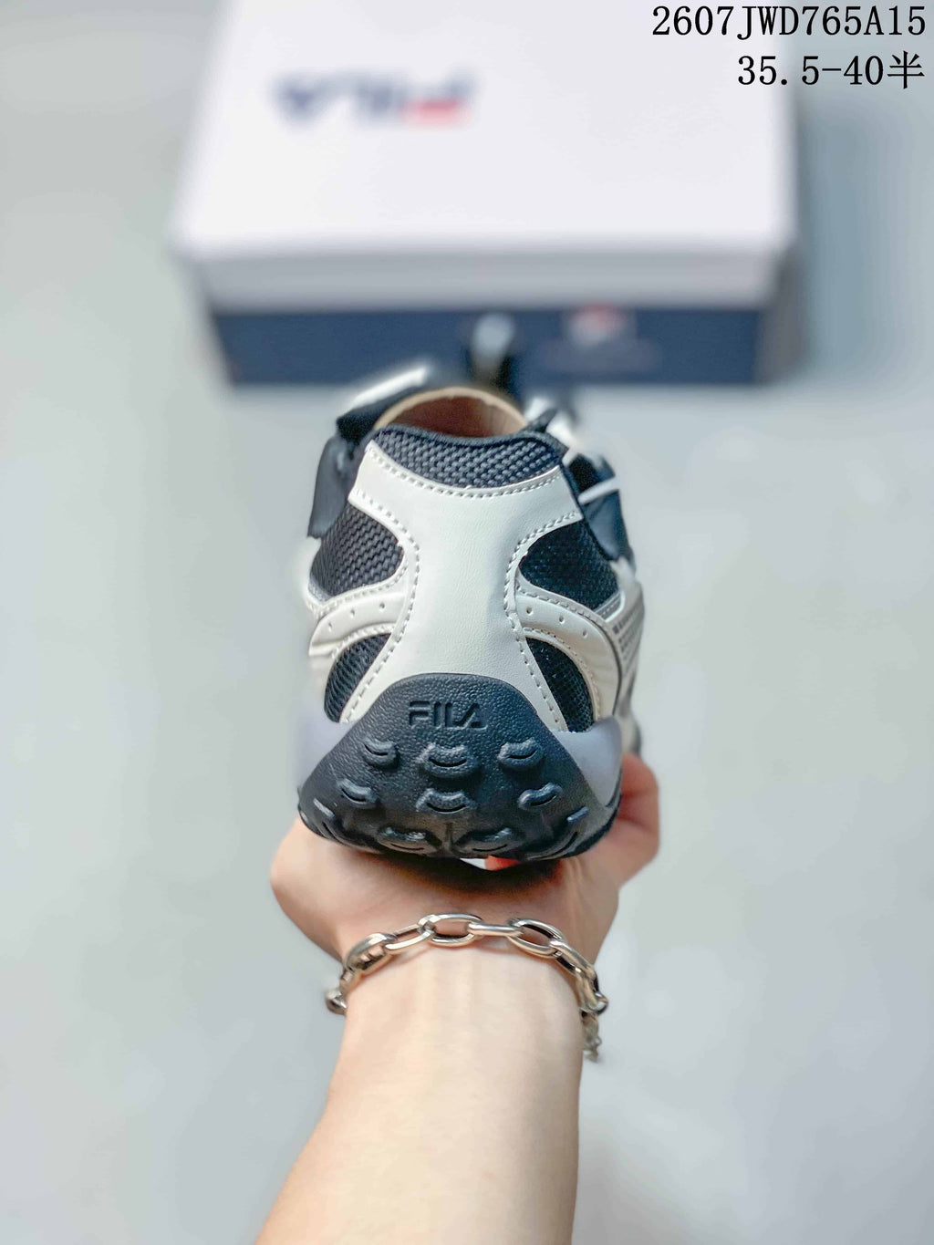 Rear view of a black-and-white FILA sneaker showing the padded heel, FILA branding, and textured outsole; overlay shows style code 2607JWD765A15 and size range 35.5–40.5.