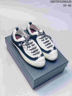 Pair of black and white low-top sneakers displayed on a dark box, showing the rounded toe, contrast panels, textured laces and side branding.