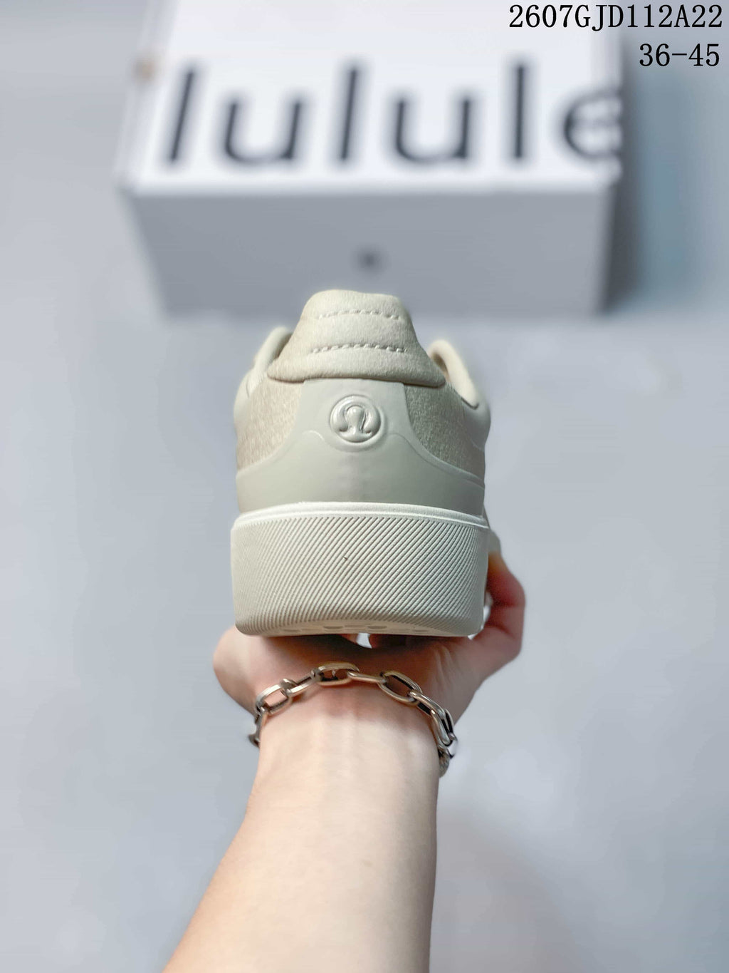 Rear view of a light neutral lululemon sneaker showing the padded heel, embossed logo and ribbed sole edge.