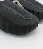 Close-up of the textured black upper, circular emblem and scalloped front edge.