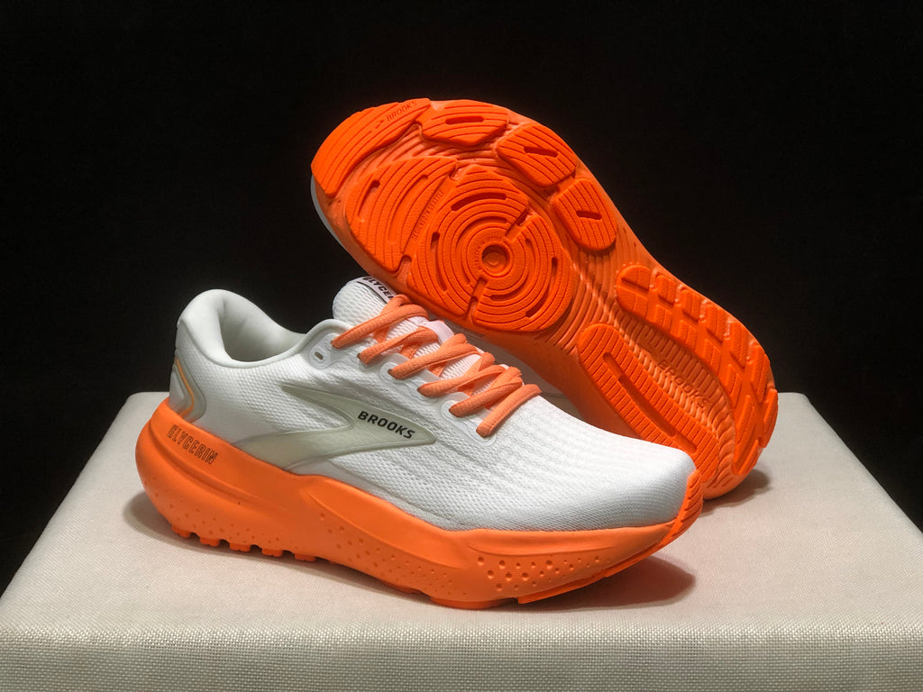 Three-quarter view of the white and orange sneakers with one shoe lifted to show the orange outsole tread.
