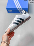 Side view of a white low-top sneaker with black adidas stripes, gray toe overlay, and gum-colored sole.