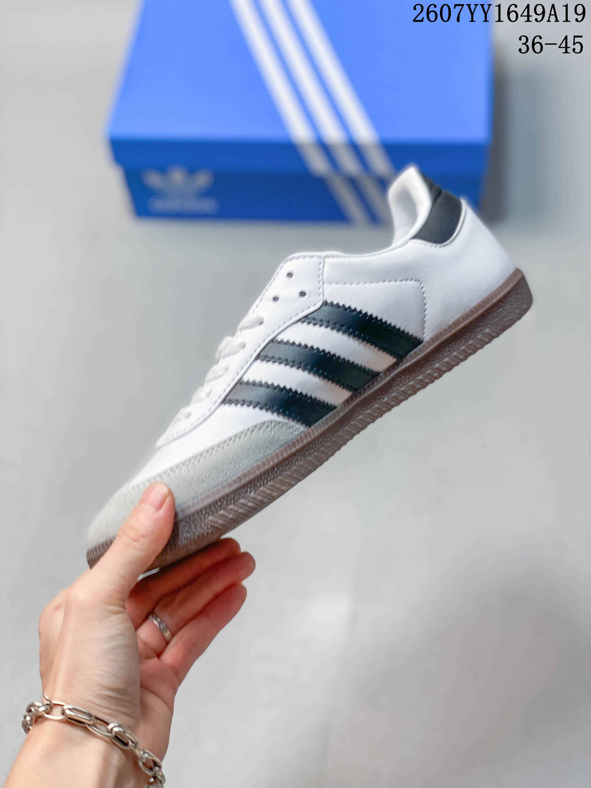 Side view of a white low-top sneaker with black adidas stripes, gray toe overlay, and gum-colored sole.