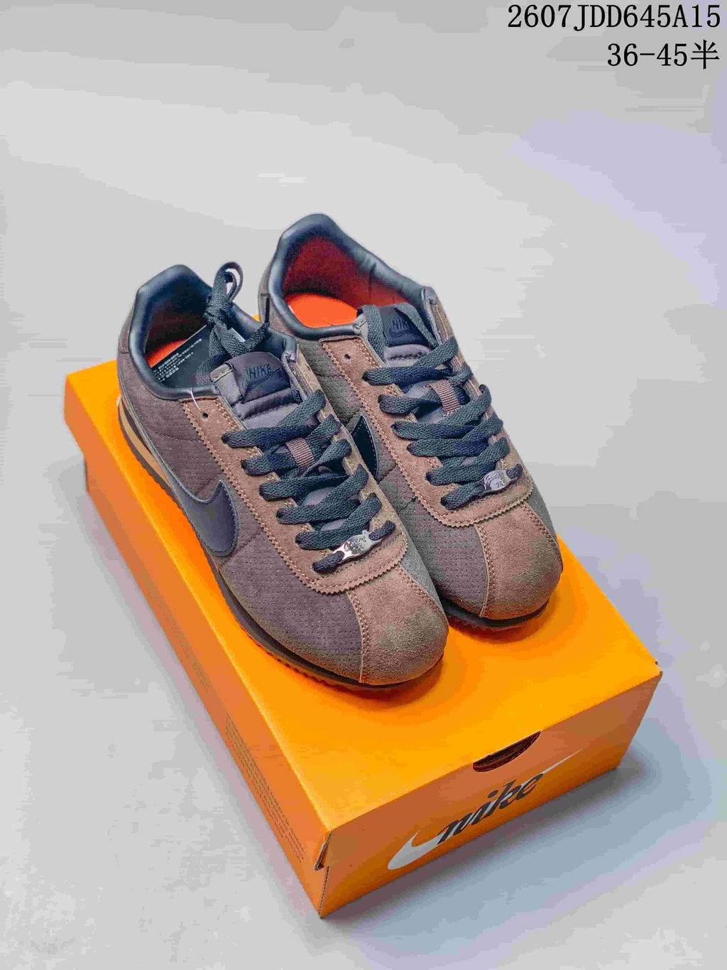 Pair of brown and black Nike sneakers displayed on an orange shoe box; overlay text shows style code 2607JDD645A15 and size range 36–45.5.