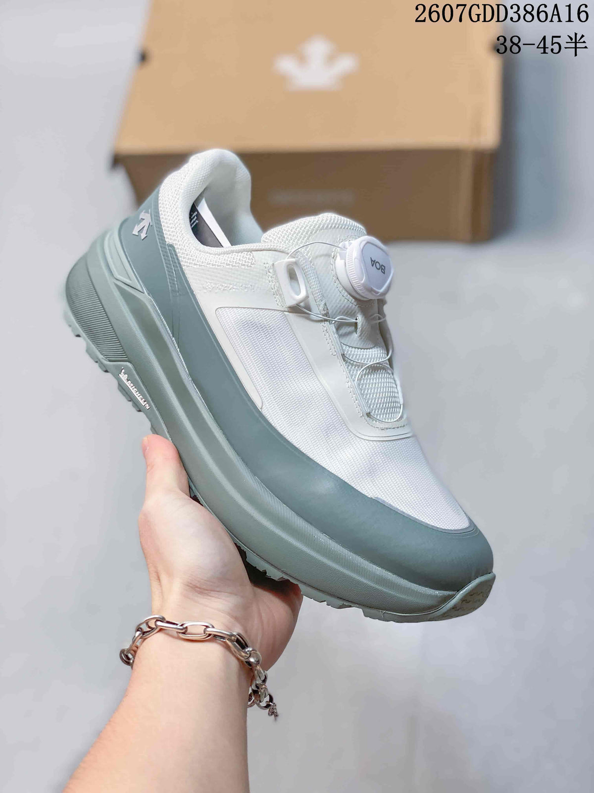 Three-quarter side view of the white and gray DESCENTE sneaker showing the dial closure, layered panels, and textured sole.