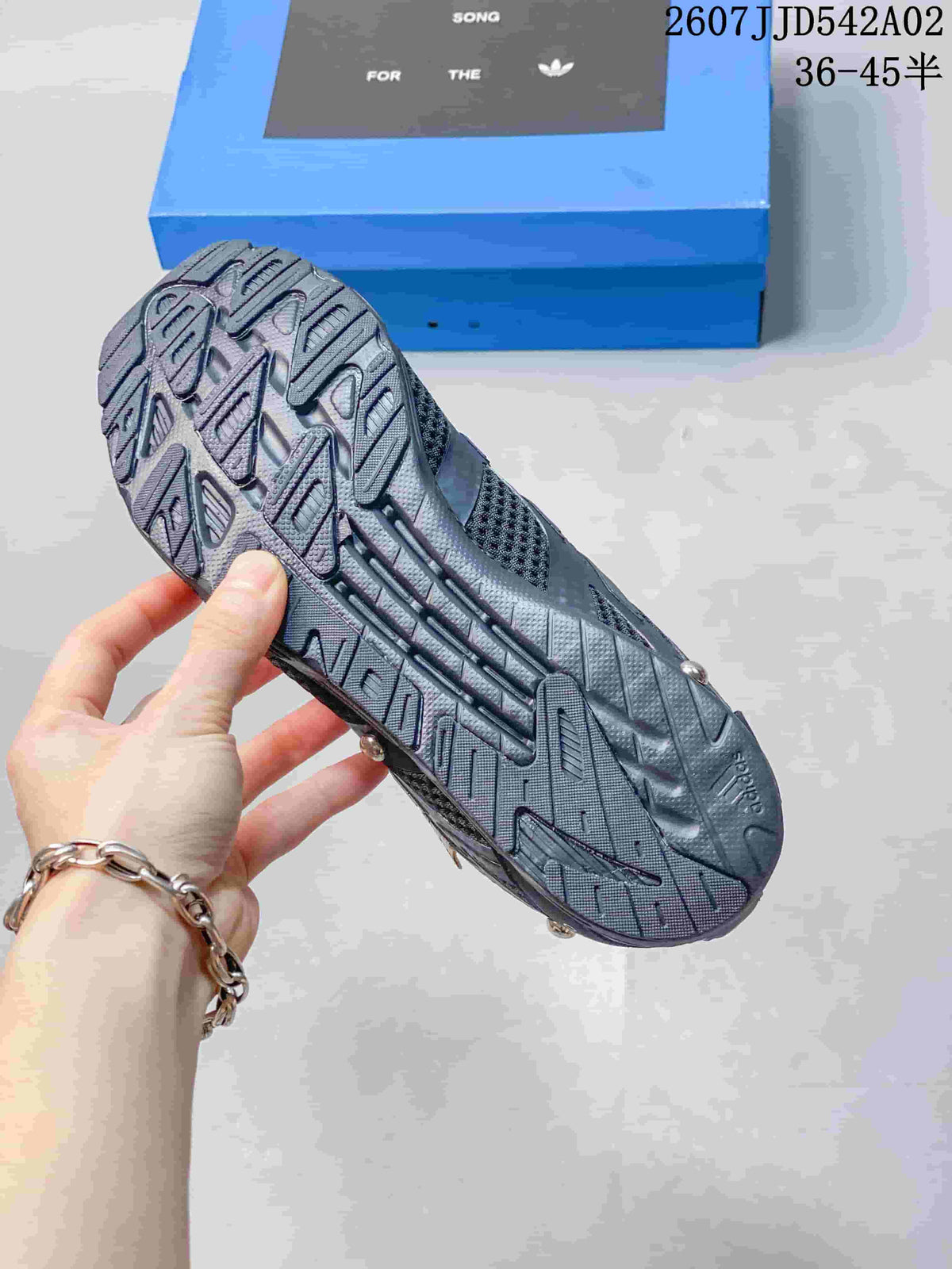 Textured outsole of a charcoal sneaker with the branded shoe box behind it