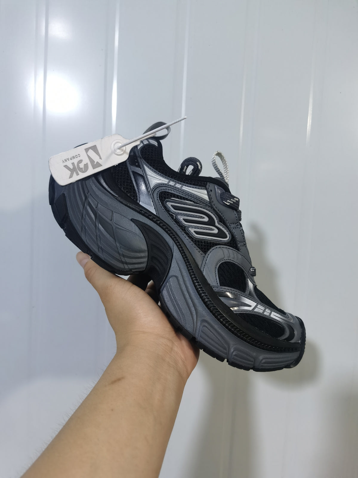 Black and grey Skechers sneaker held at an angle, showing mesh panels, layered side detailing, and a sculpted sole.