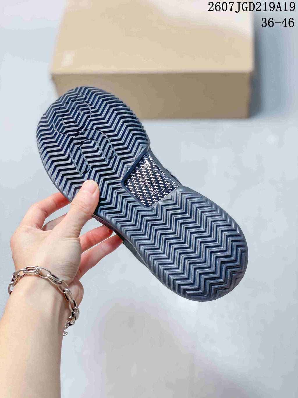 View of the black tennis shoe outsole showing its zigzag tread pattern, with a box behind it.