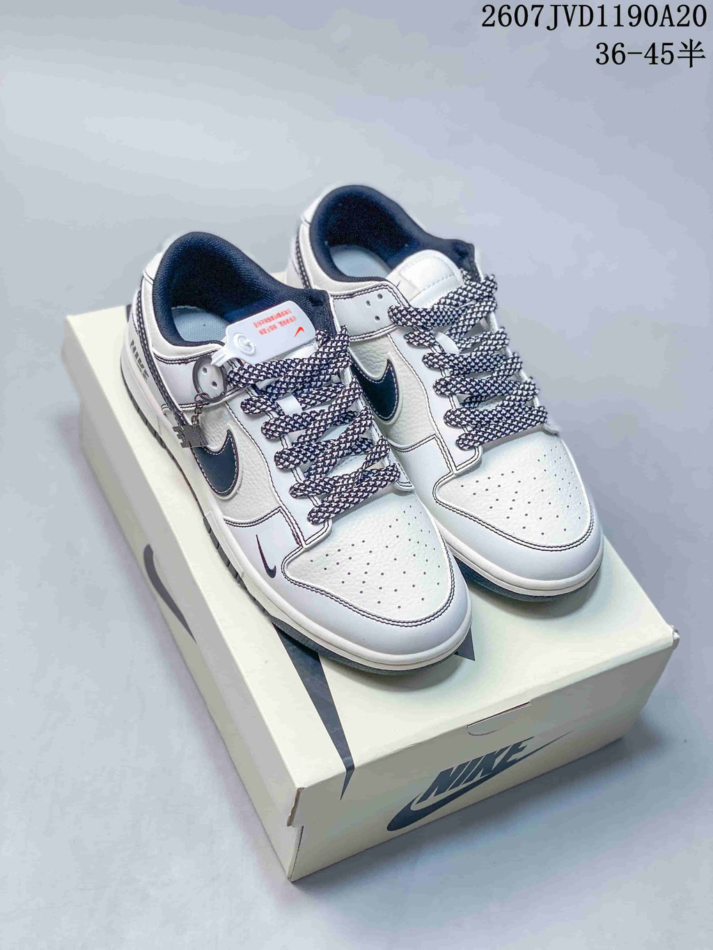 Pair of off-white and black Nike SB Dunk Low sneakers displayed on a Nike shoe box, with patterned laces and contrasting Swoosh details.