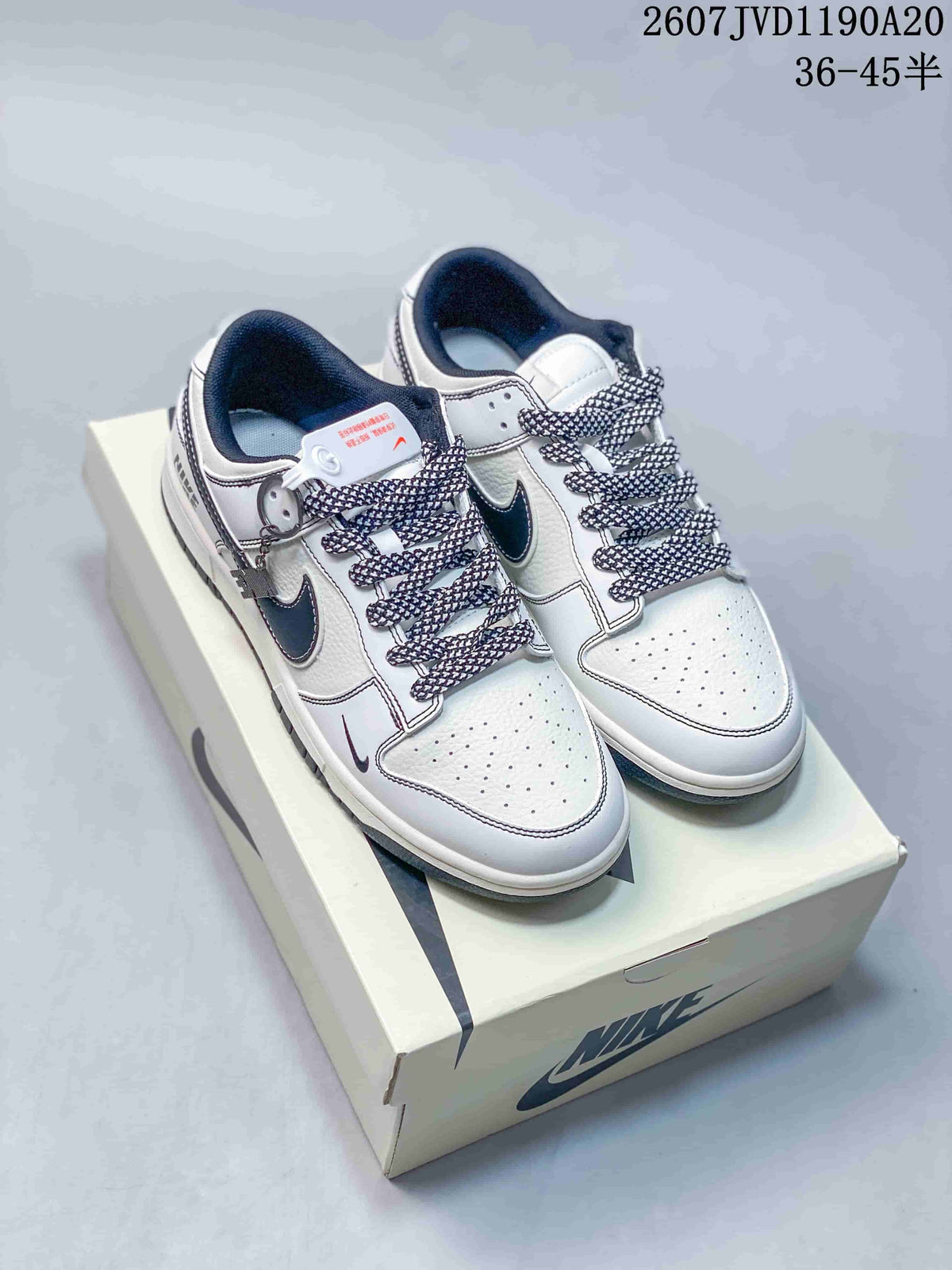 Pair of off-white and black Nike SB Dunk Low sneakers displayed on a Nike shoe box, with patterned laces and contrasting Swoosh details.