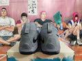 Rear view of gray Nike basketball shoes with black Swoosh logos and speckled heel panels