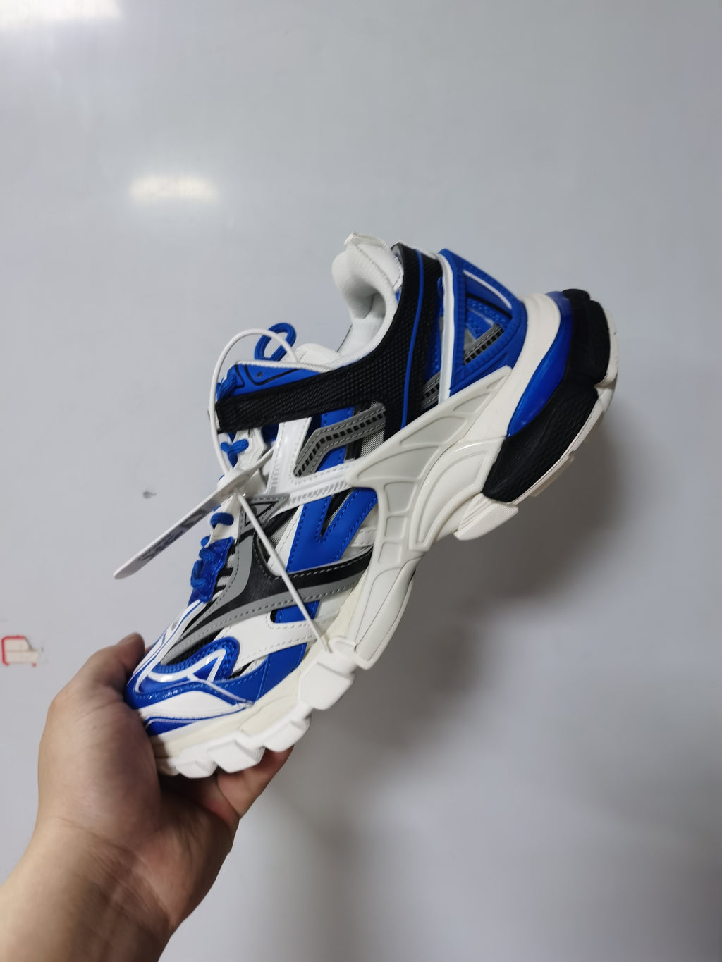 Side and top view of the white and royal-blue Balenciaga Track.2 open sneaker being held by hand.