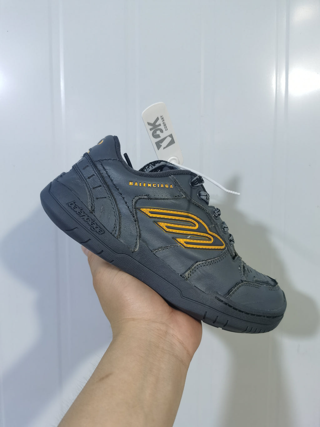 Angled rear-side view showing the Balenciaga branding, layered panels, yellow side detail, and dark outsole.